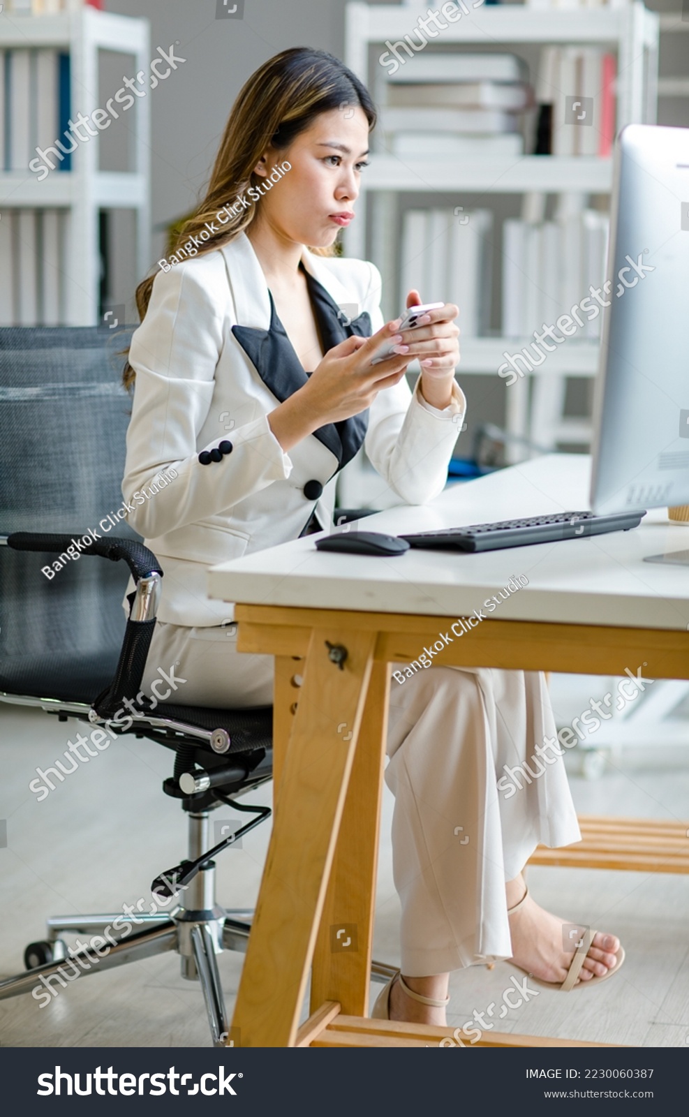 Asian female businesswoman search computer information while uesing mobile phone. Manager agent solve help to company customer distantly modern tech usage, busy fruitful workday concept #2230060387