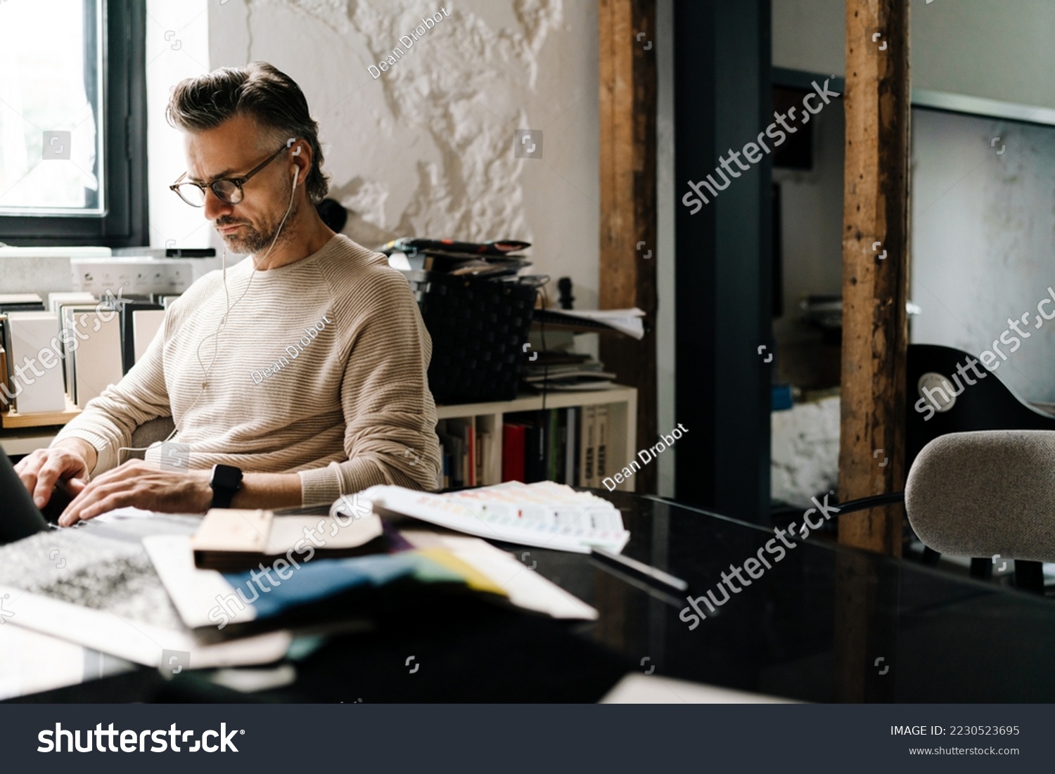 White middle-aged man in earphones using laptop computer while sitting in modern office #2230523695