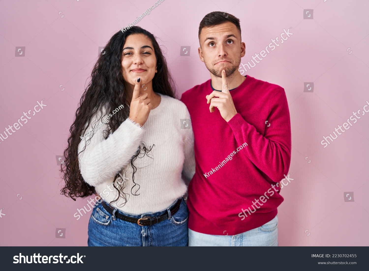 Young hispanic couple standing over pink background thinking concentrated about doubt with finger on chin and looking up wondering  #2230702455