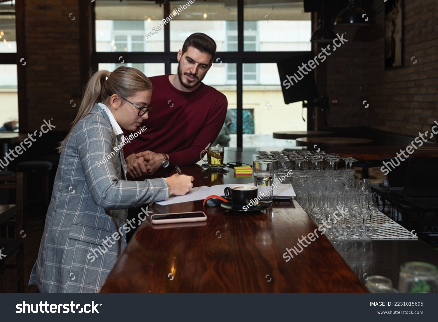 Health inspector sitting in a restaurant and writes a fine and a negative report to the owner or manager of the cafeteria after she finds poor hygiene conditions in the kitchen.  #2231015695