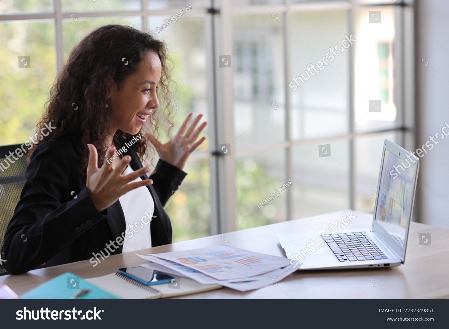 Attractive professional latin female employee worker sitting, using laptop computer with smart mobile phone at home workplace. Businesswoman working on paperwork while looking at camera and smile #2232349851