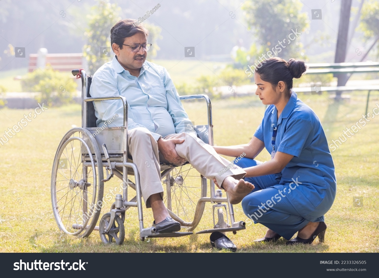 Female caregiver helping senior man in wheelchair to lift lag at park. #2233326505