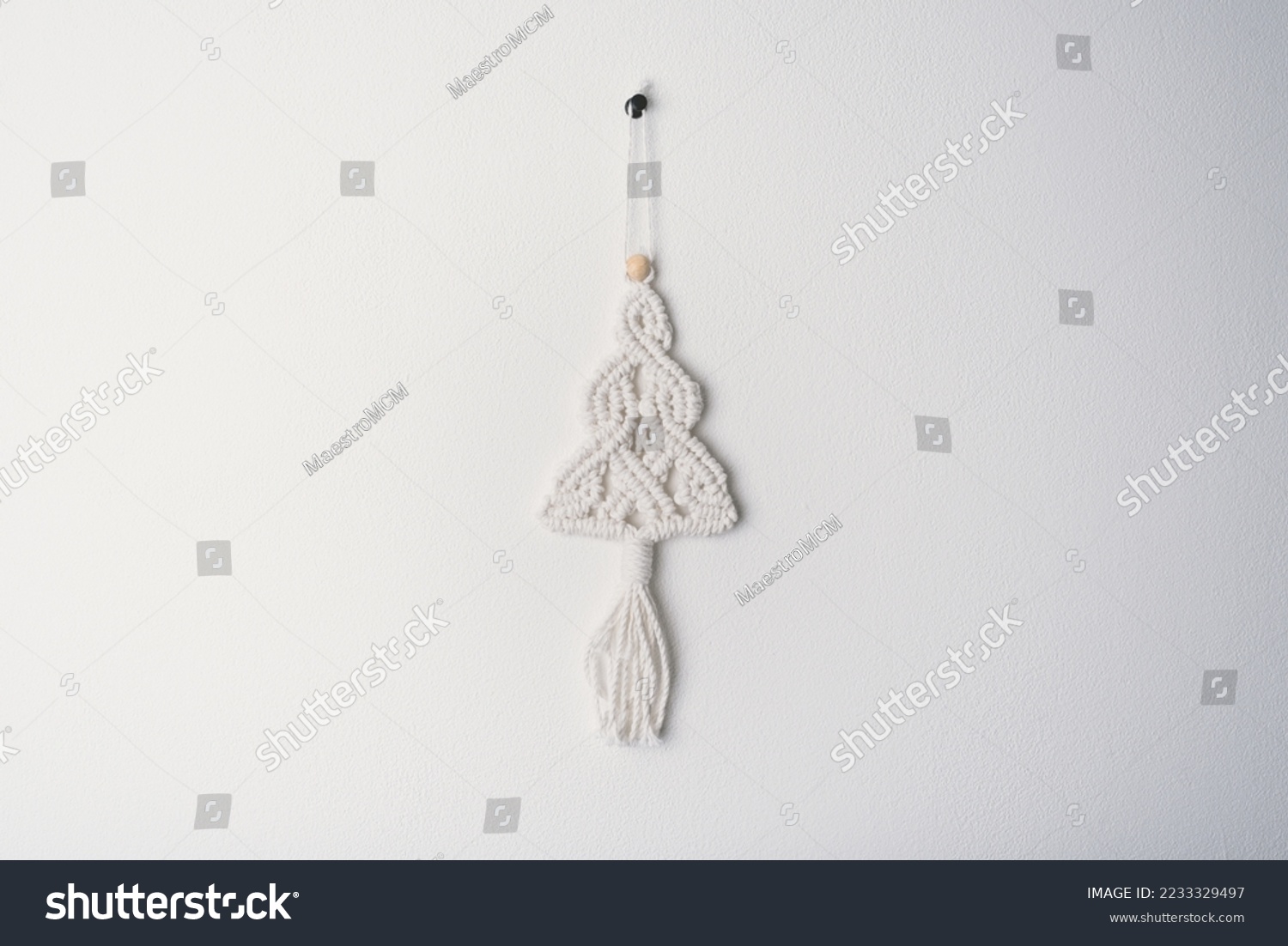 Christmas handmade macrame tree ornament winter holiday, white eco macramé Christmas tree decorations in boho style hanging. tree made from cotton white string pattern on white wall background  #2233329497