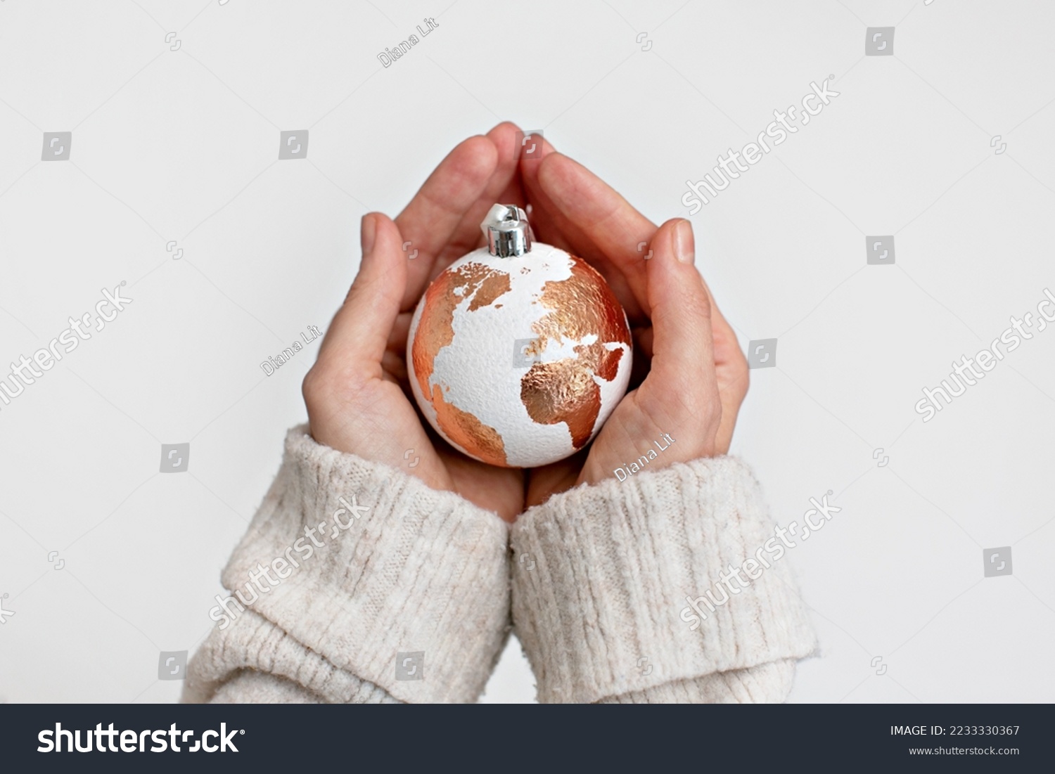 White Christmas ball in the form of a globe with a gold leaf holding carefully with two hands. The concept of caring for our planet. Solving problems in the new year. Hope and wish for peace on Earth. #2233330367