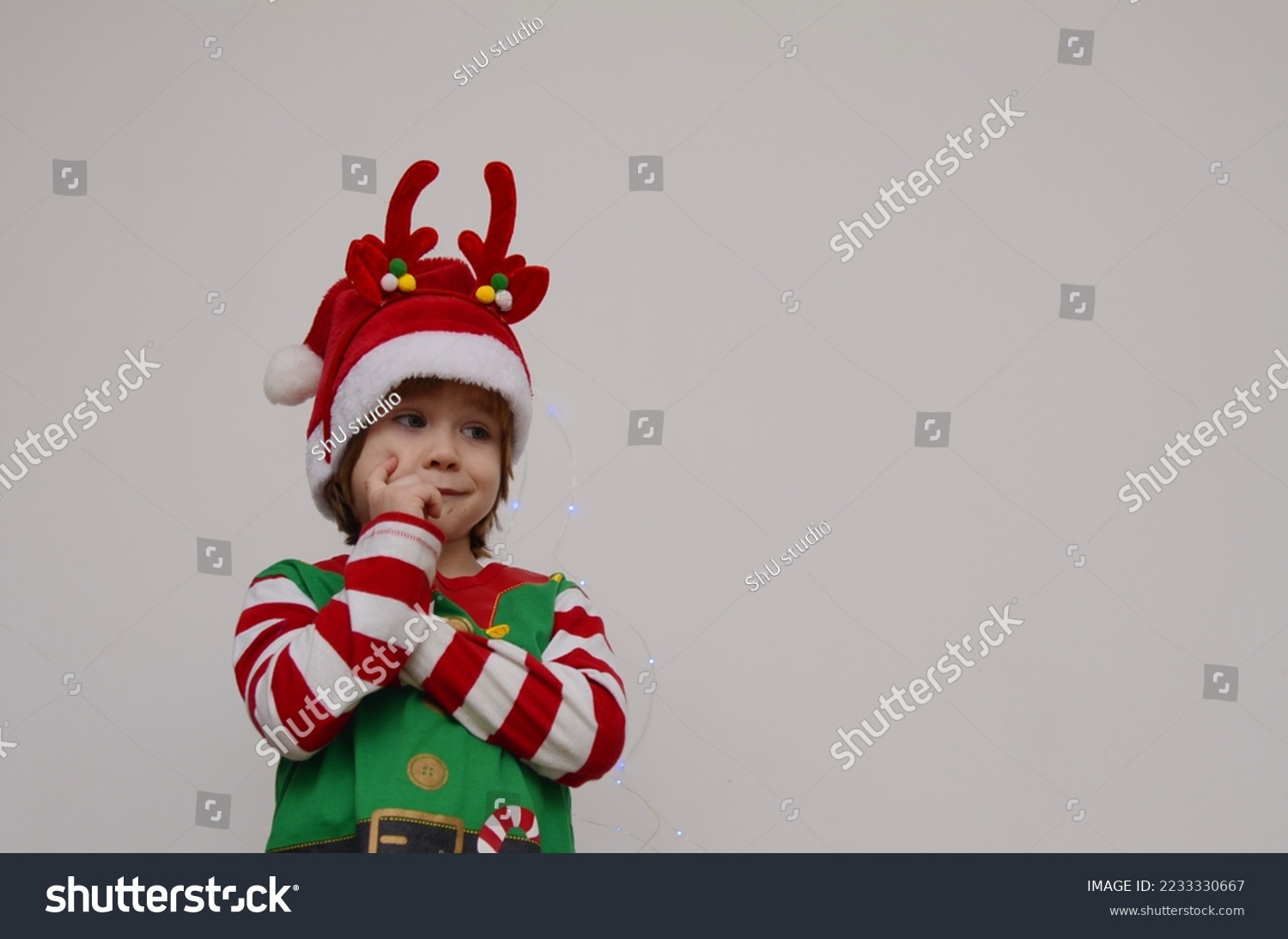 Child in Santa's hat, hand near face, Christmas waiting pose. Isolate on white, space for text #2233330667