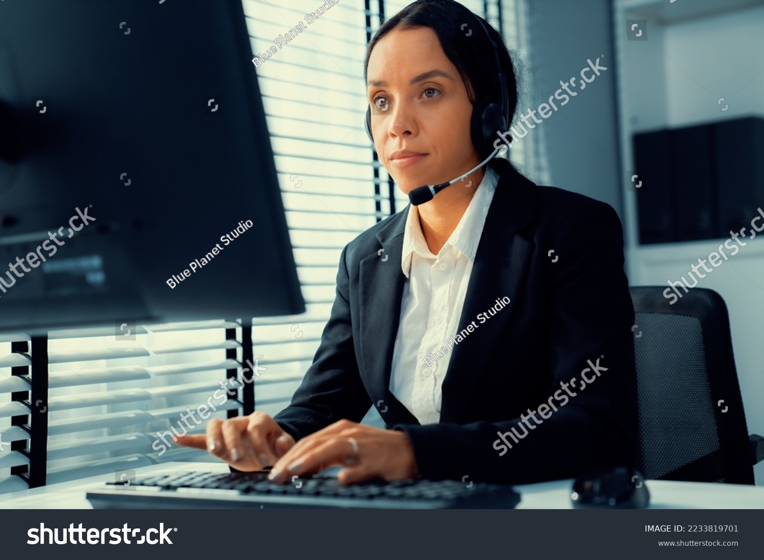Competent female operator working on computer and talking with clients. Concept relevant to both call centers and customer service offices. #2233819701