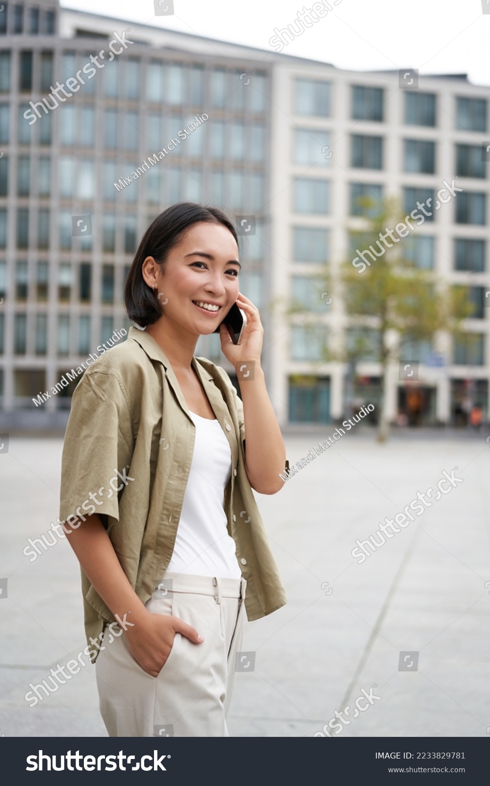 Modern young asian girl talks on mobile phone, uses telephone on city street. Woman smiling while calling someone on smartphone. #2233829781