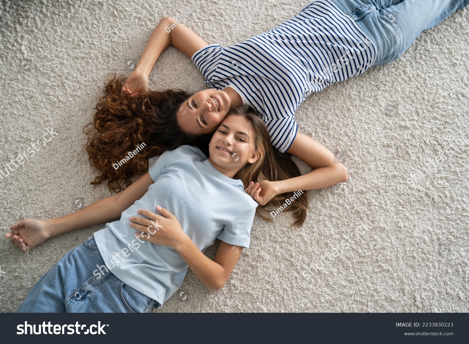 Satisfied relaxed woman nanny and teen girl both lie on floor in apartment and smiled look at camera top view. Happy close-knit family life of mother and daughter of school age dressed in casual style #2233830223