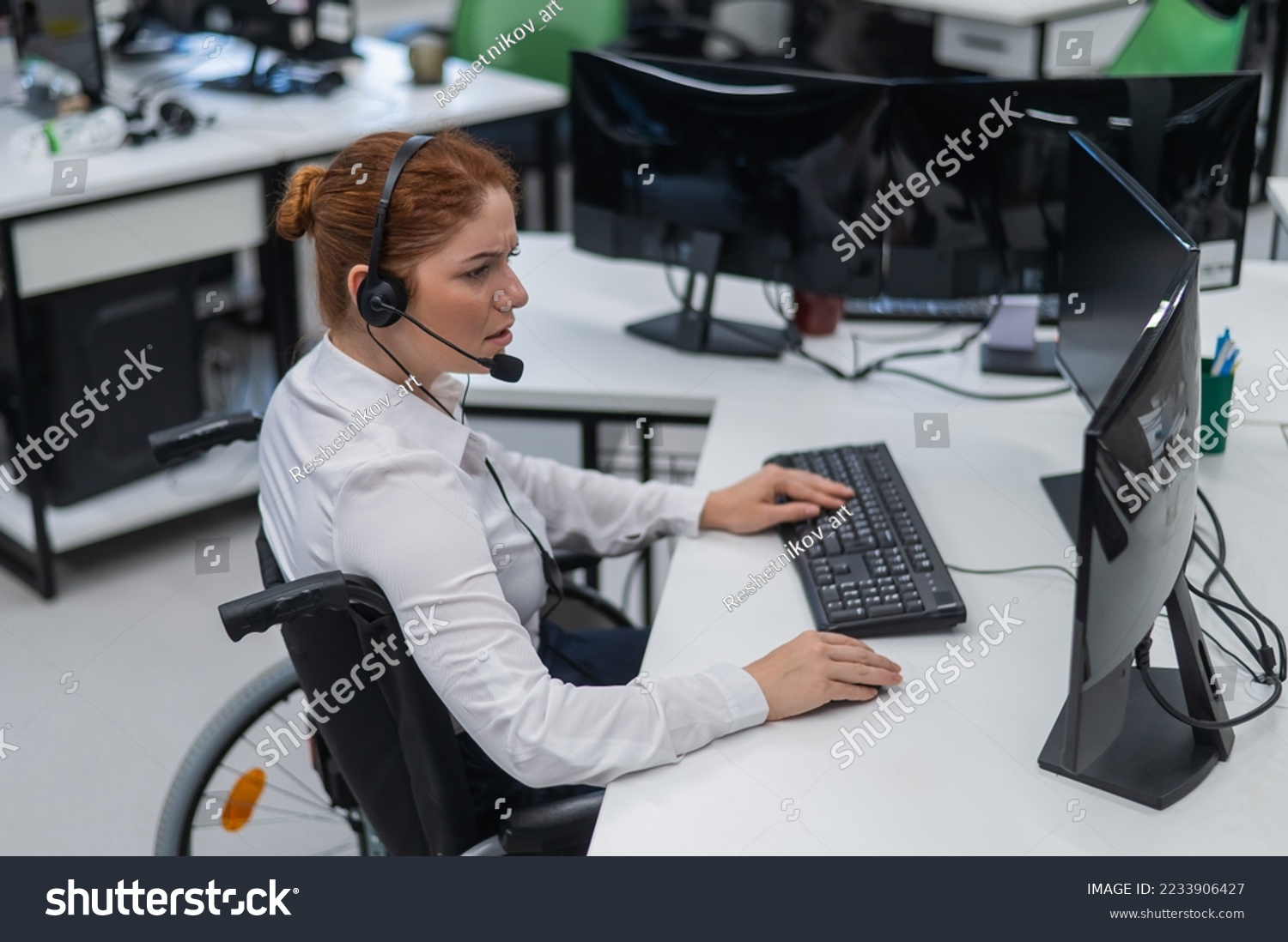 Red-haired caucasian woman in a wheelchair talking on a headset. Female call center worker at her desk. #2233906427