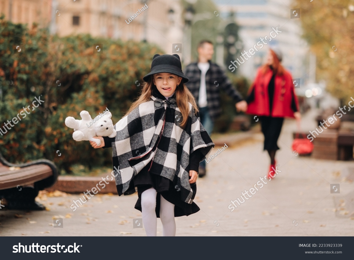 A little girl with her parents runs to the autumn city.A stylish family of three strolls through the autumn city #2233923339