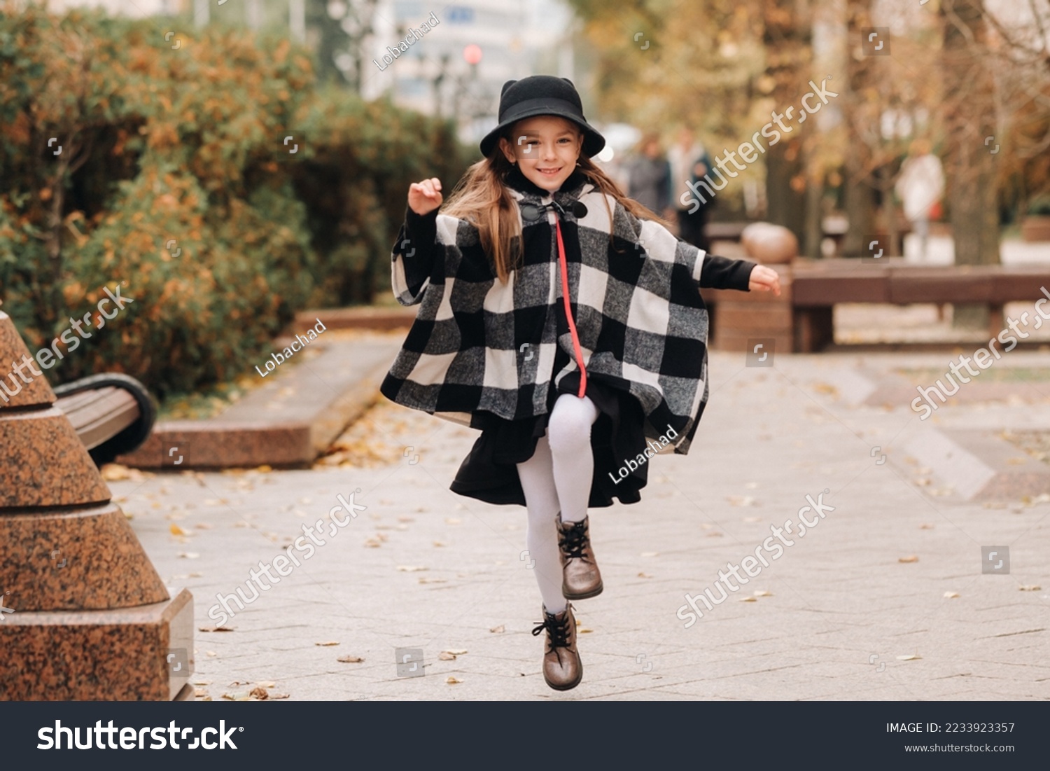 A stylish little girl in a hat walks around the autumn city #2233923357