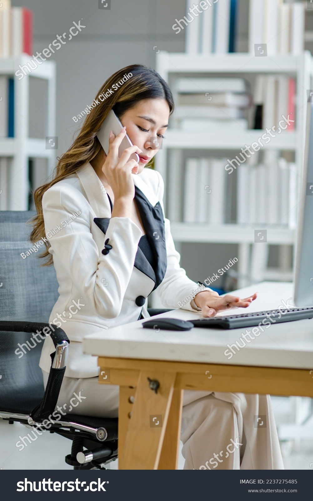 Asian female businesswoman search computer information while talking with client mobile phone. Manager agent solve help to company customer distantly modern tech usage, busy fruitful workday concept #2237275485
