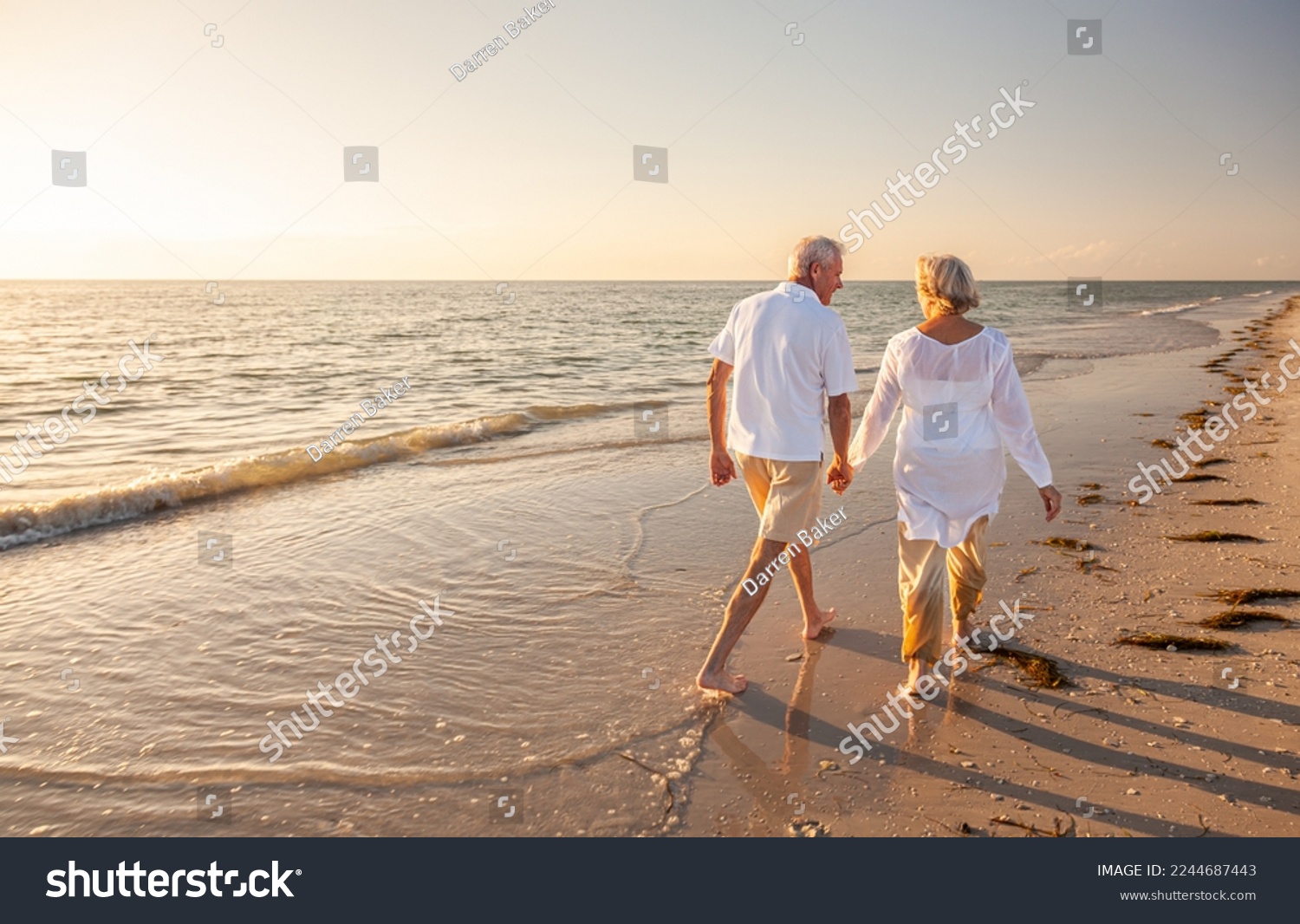 Happy senior man and woman old retired couple walking and holding hands on a beach at sunset, s3niorlife #2244687443