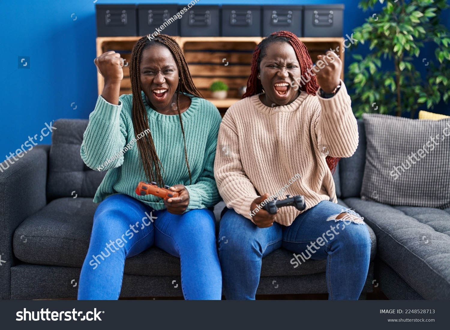 Two african woman playing video game holding controller annoyed and frustrated shouting with anger, yelling crazy with anger and hand raised  #2248528713