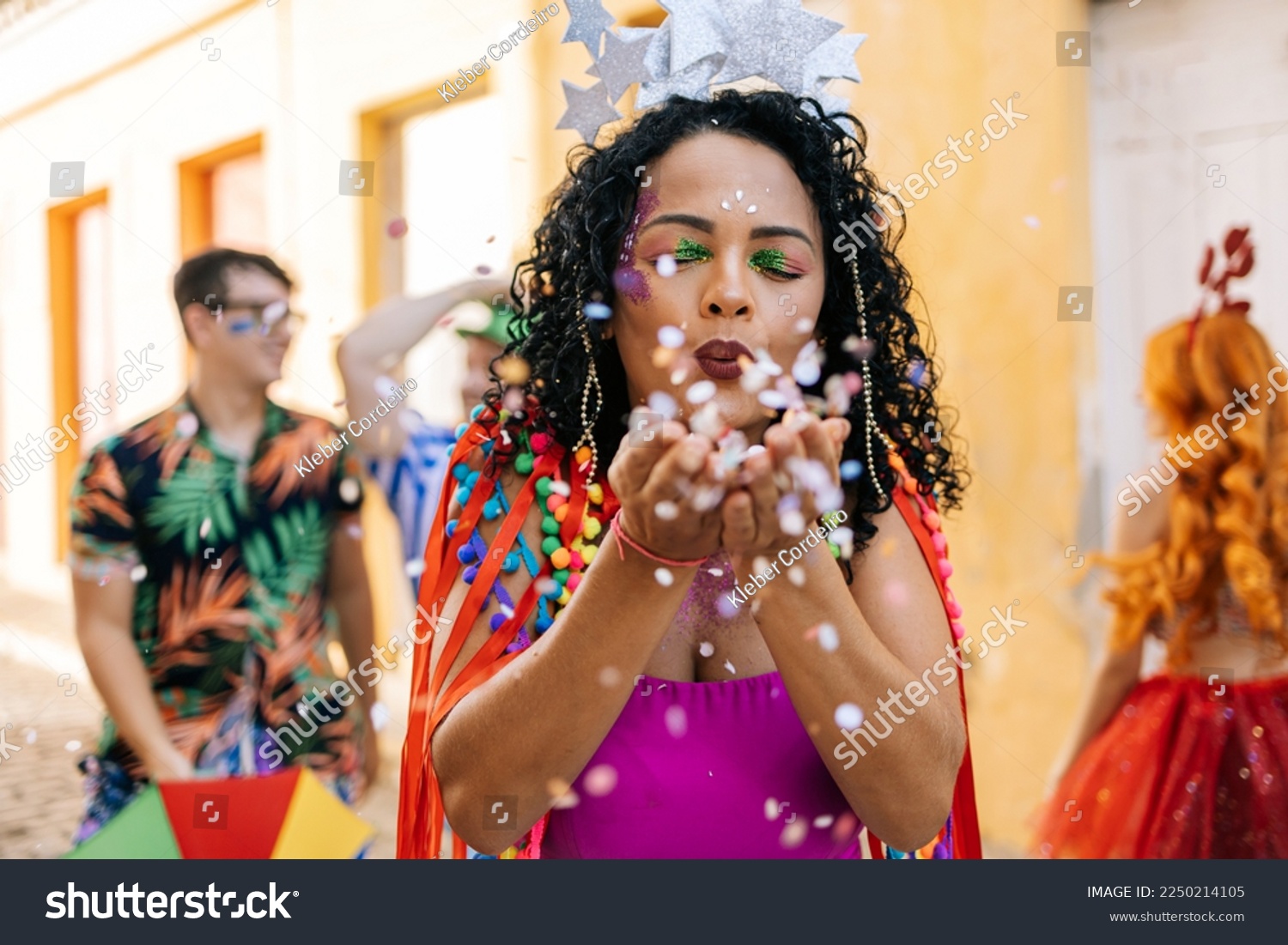 Brazilian Carnival. Young woman enjoying the carnival party blowing confetti #2250214105