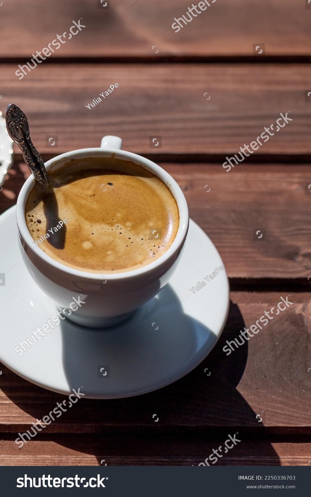 Cup of coffee with spoon on table. White porcelain cup on saucer. Copy space.Black Coffee in natural sun light.espresso on rustic wooden table. good morning concept #2250336703