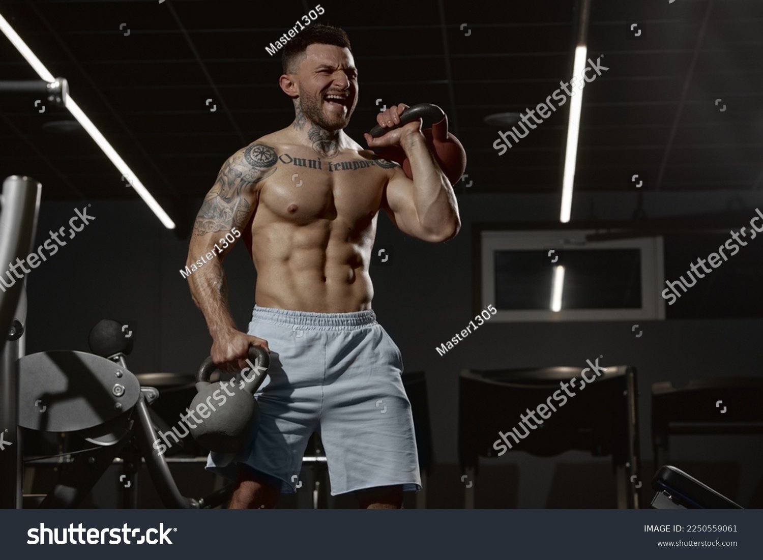 Portrait of young muscular man training shirtless in gym indoors. Hand exercises with kettlebell. Relief body shape. Concept of health, sportive lifestyle, fitness, body care, diet, strength #2250559061