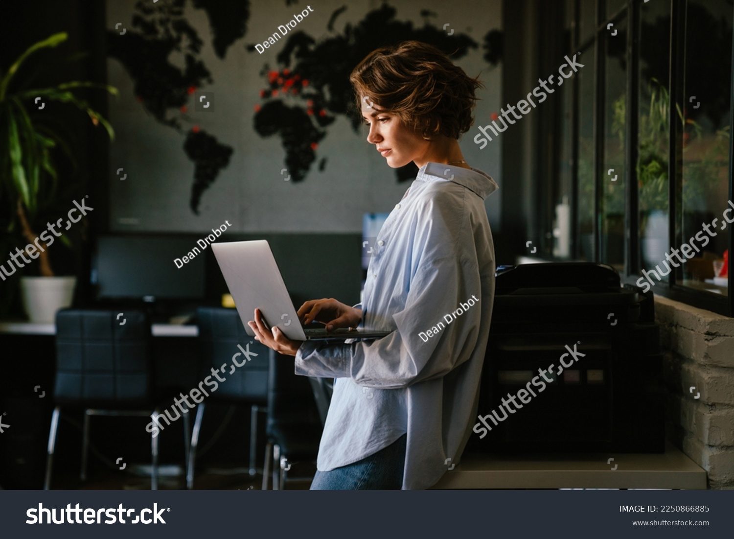 Beautiful young concentrated business woman wearing shirt using laptop while standing in modern workspace #2250866885