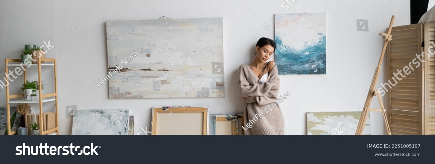 Sexy short haired artist in bra and sweater standing in workshop, banner #2251005197