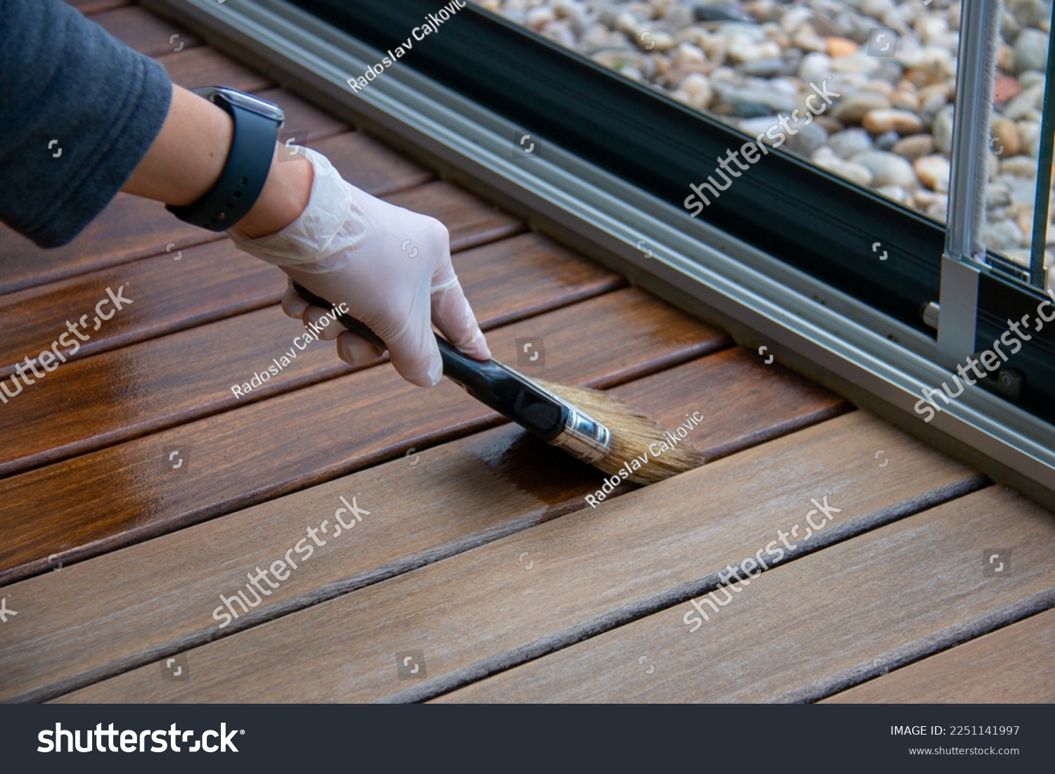 Deck staining, worker applying deck oil on decking boards with paint brush, hardwood terrace renovation #2251141997