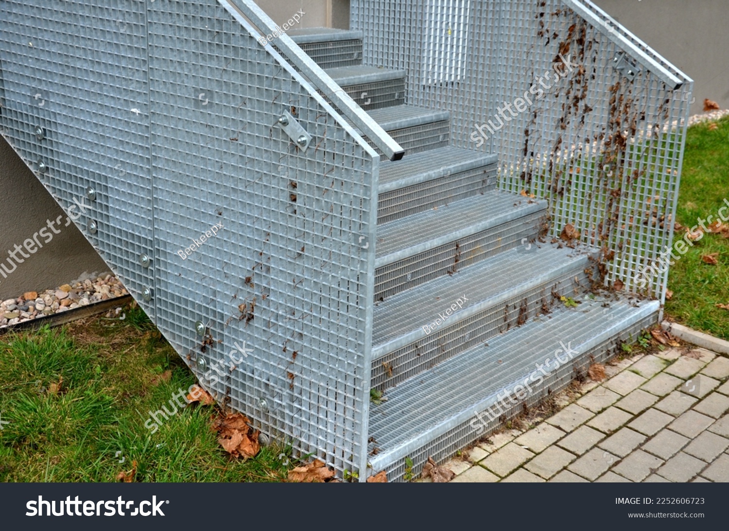 Stairs to a residential building made of stainless steel grid. galvanized stair grating made of expanded metal. lawn concrete sidewalk.  #2252606723
