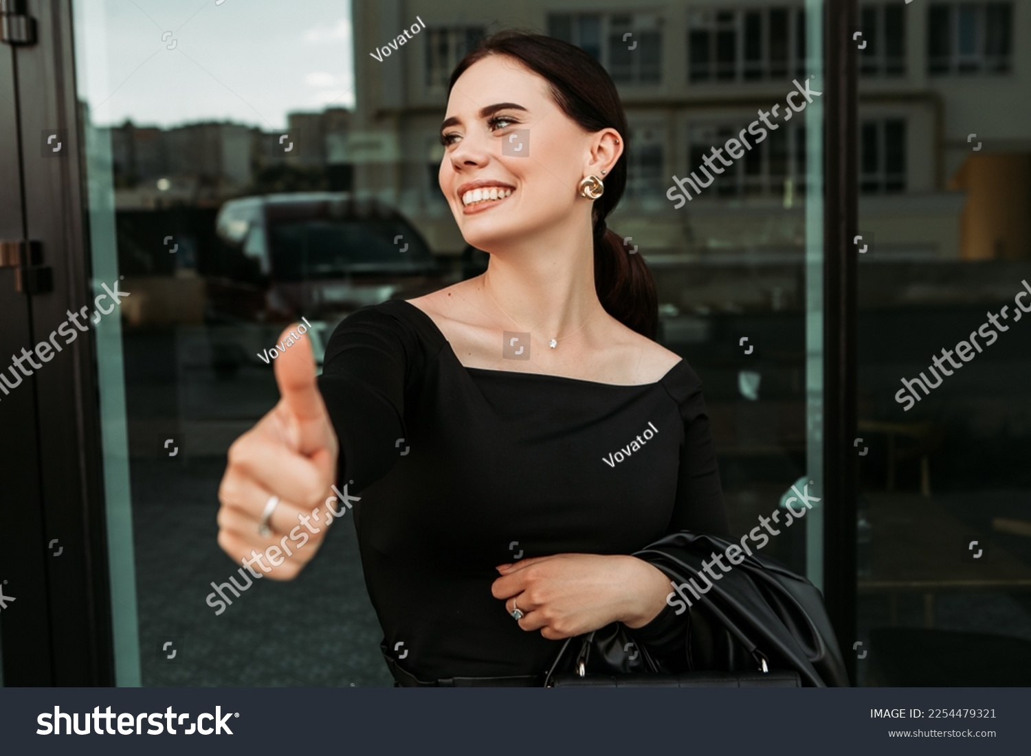 Pretty brunette caucasian woman standing outside street with white teeth beaming healthy smiling lady. Happy millennial girl showing thumb up like OK approve positive sign gesturing making faces

 #2254479321