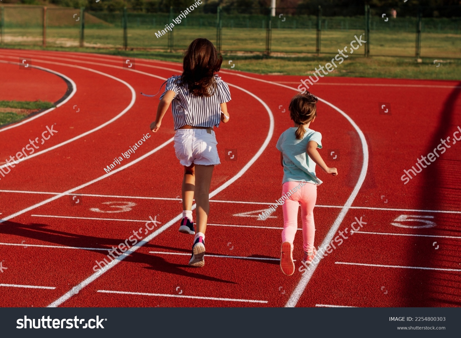 Two small girls running on outdoor track during summer day #2254800303