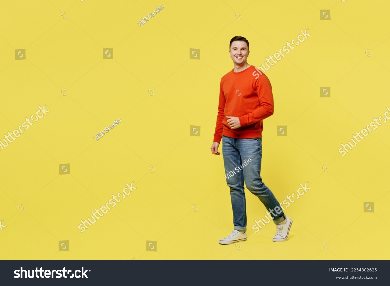 Full body profile young smiling caucasian happy cheerful man wear orange casual clothes walking going look camera isolated on plain yellow color background studio portrait. People lifestyle concept #2254802625