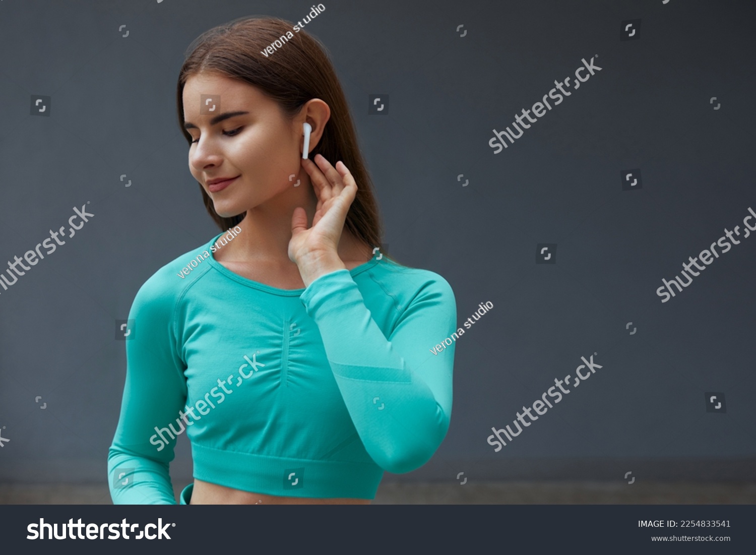 Close up portrait of beautiful young fitness girl listening to music using wireless earbud. Woman usings earphones. #2254833541