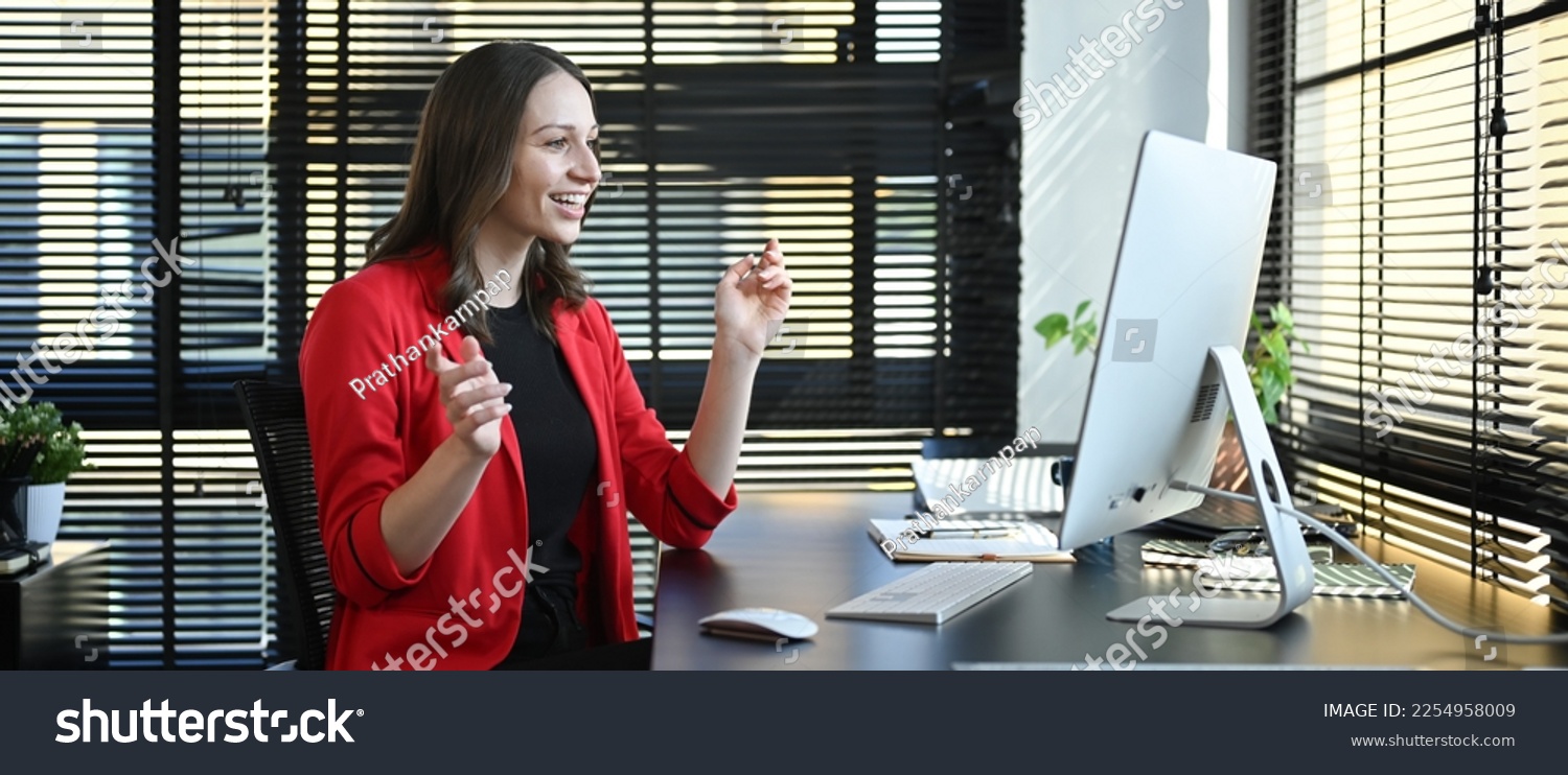 Side view of caucasian woman corporate CEO in red luxury suit watching online webinar on computer in modern office #2254958009
