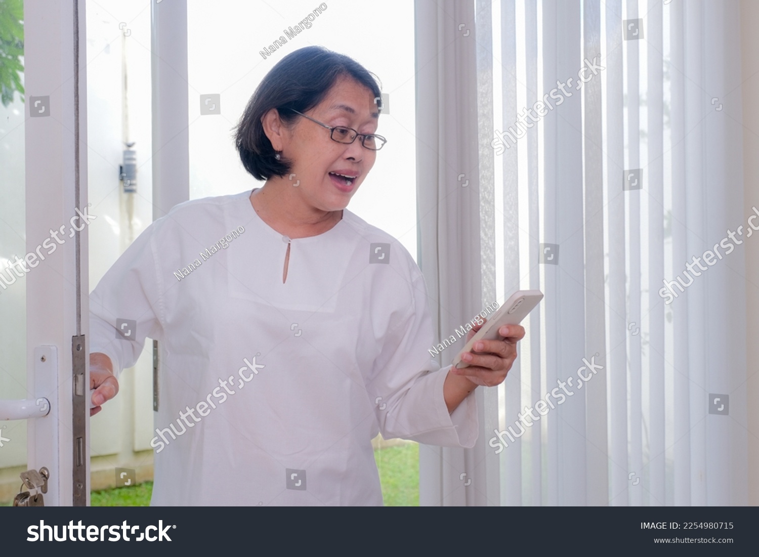 A woman answering a phone call while coming into the house.  #2254980715