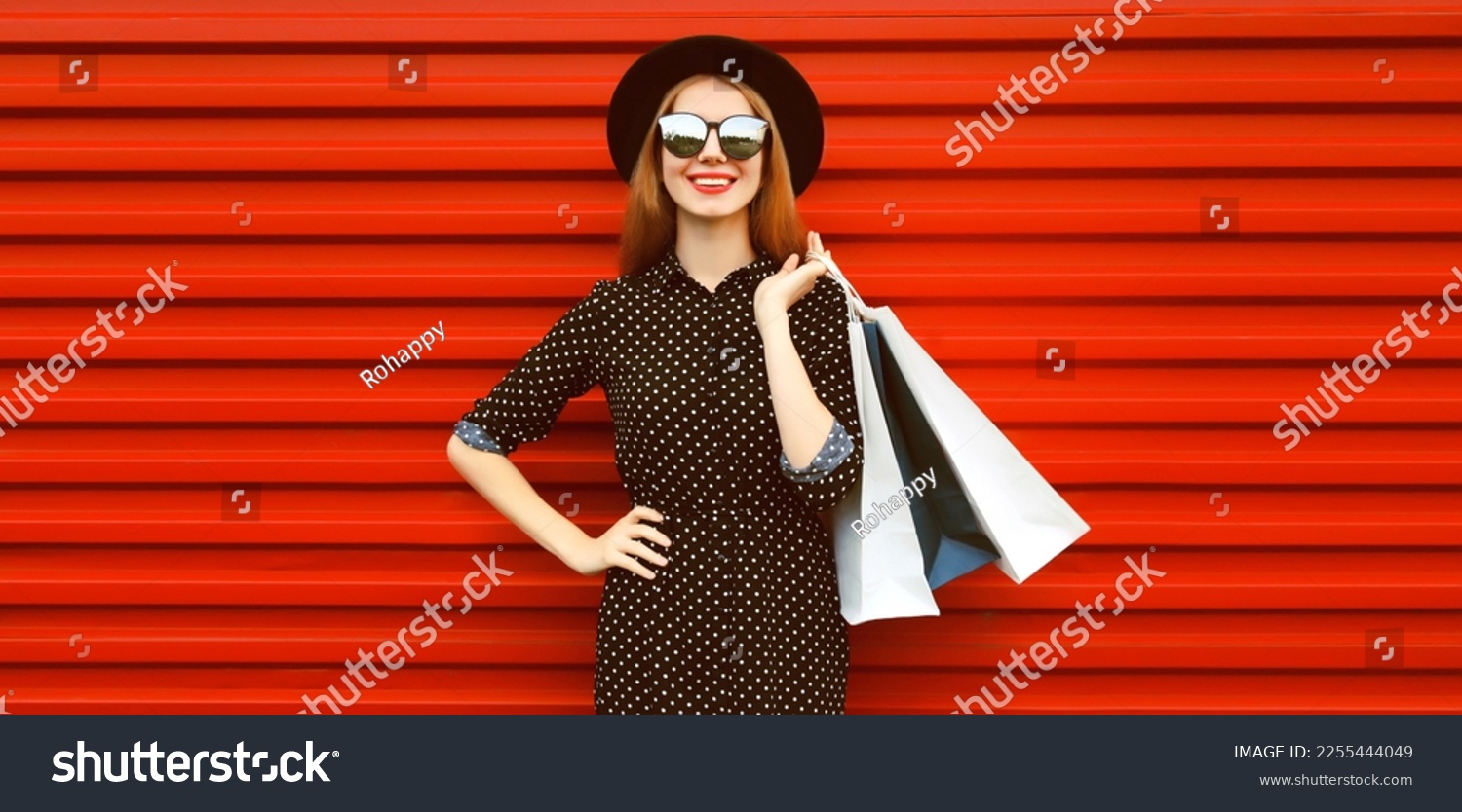 Portrait of happy smiling young woman with shopping bags wearing black round hat on red background #2255444049