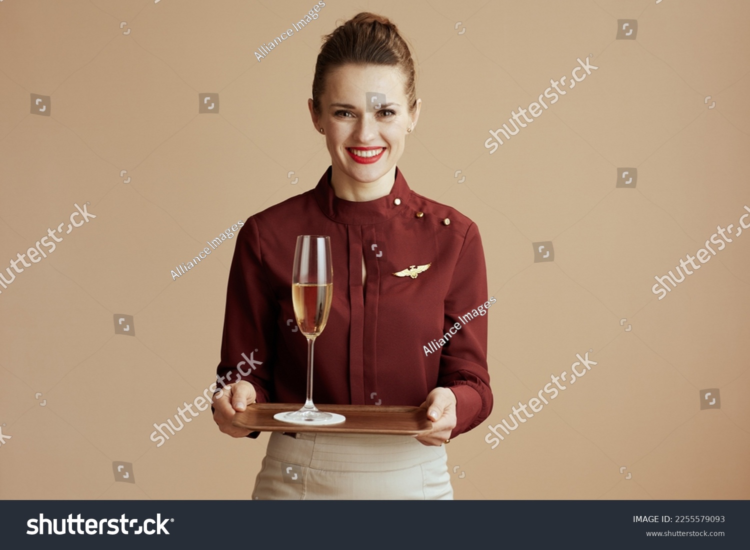 happy stylish flight attendant woman against beige background with a glass of champagne. #2255579093