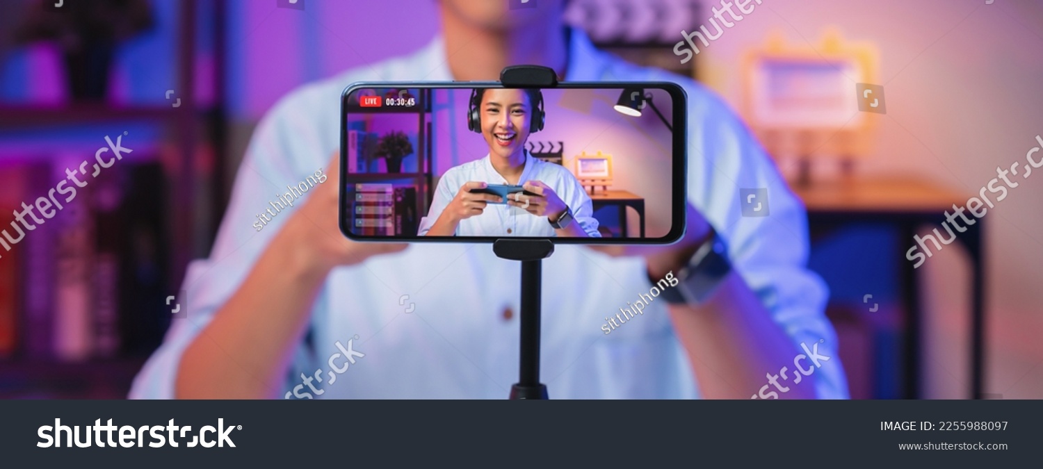 Vlogger live streaming podcast review on social media, Young Asian woman use microphones wear headphones with smartphone record video. Content creator concept. #2255988097