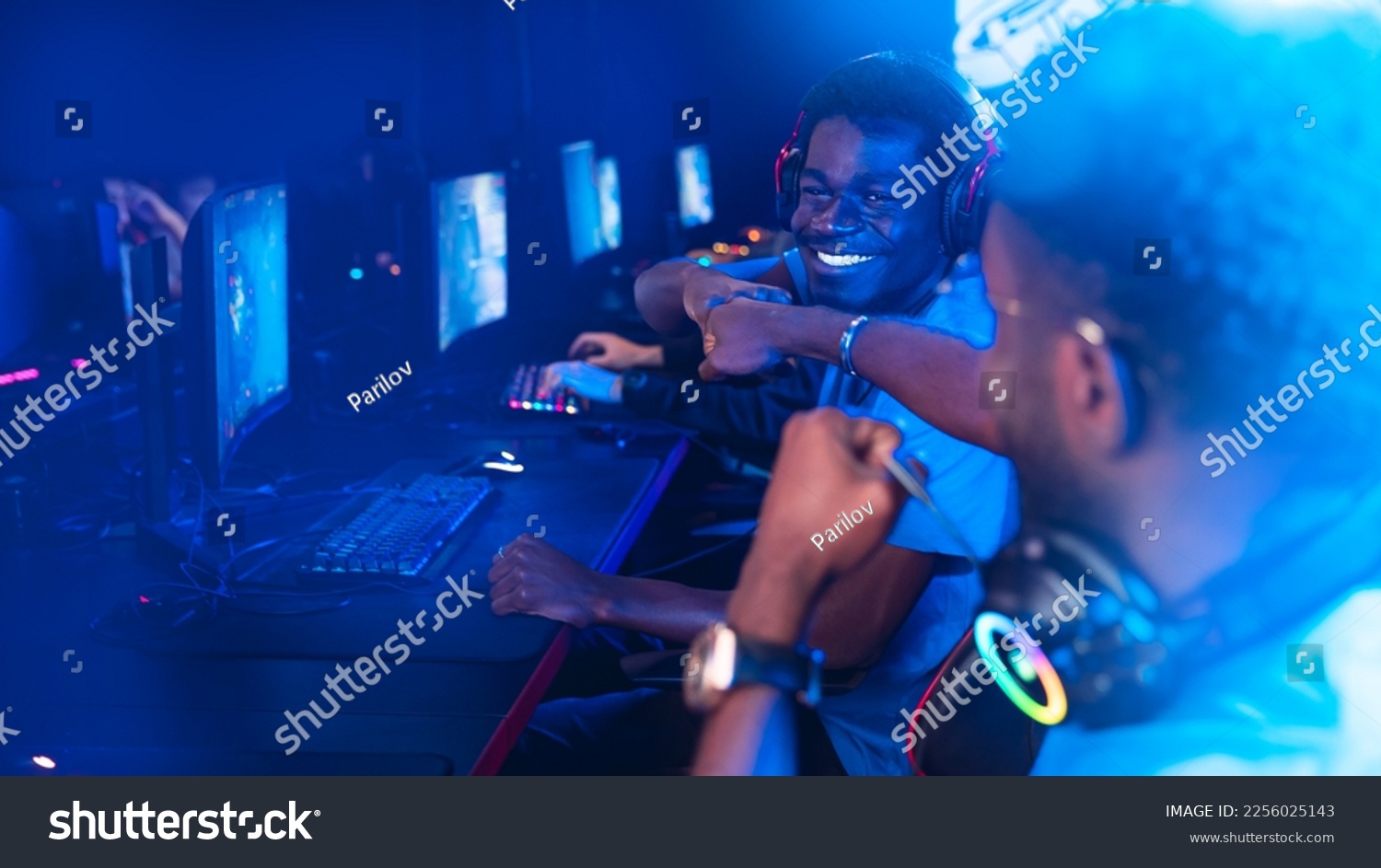 Professional african cyber gamer greeting and support team fists hands online game in neon color blur background. #2256025143