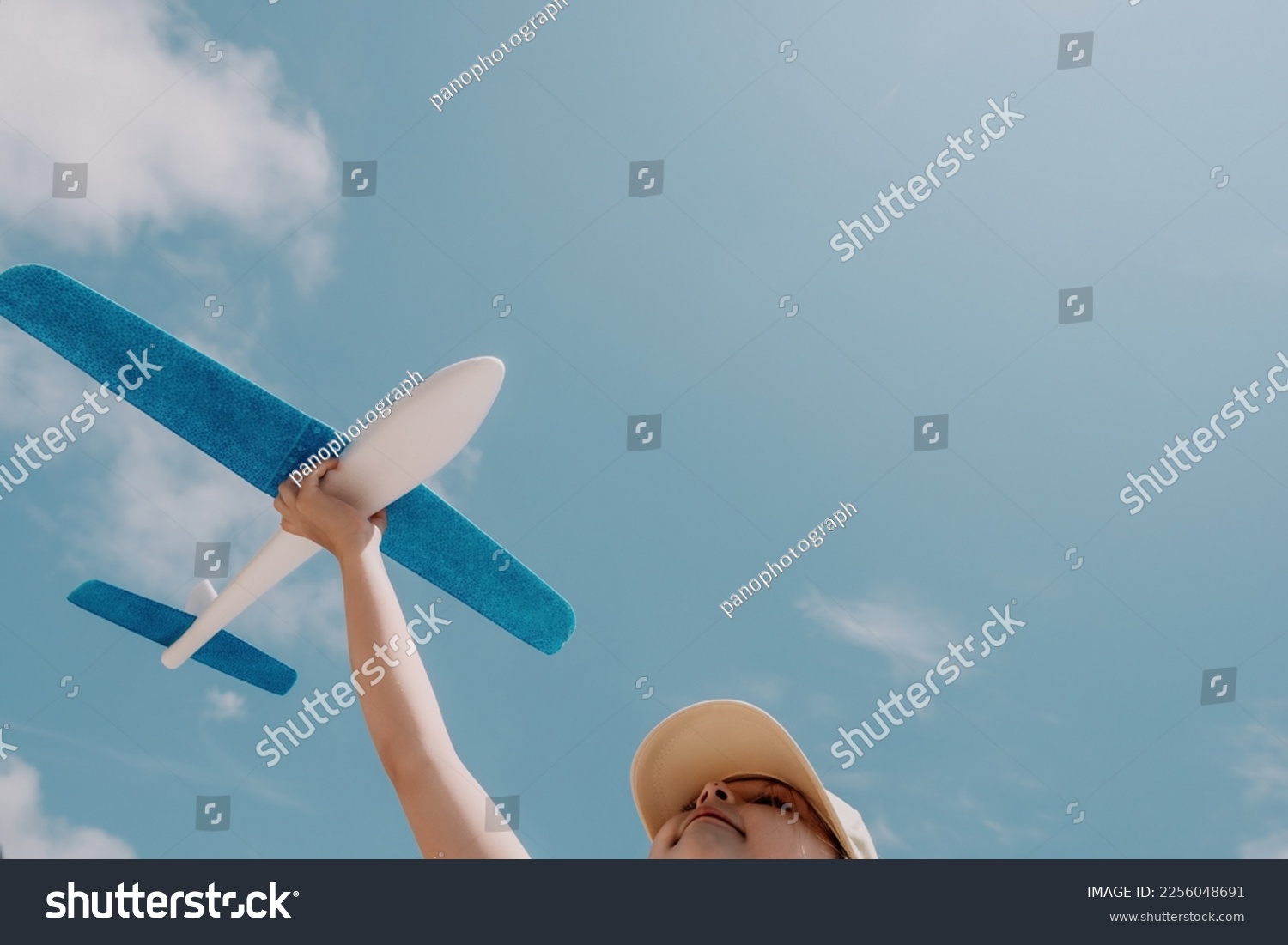 Kid playing with toy airplane. Children dream of travel by plane. Happy child girl has fun in summer vacation by sea and mountains. Outdoors activities at background of blue sky. Lifestyle moment. #2256048691
