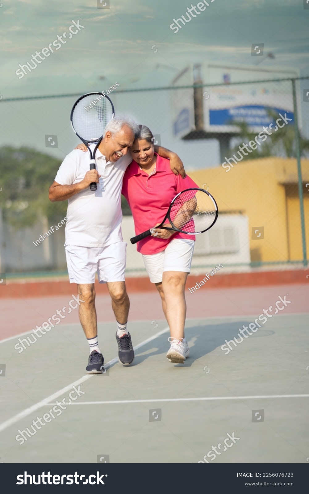 Senior man and woman hugging after playing a game of tennis at an outdoor court. #2256076723