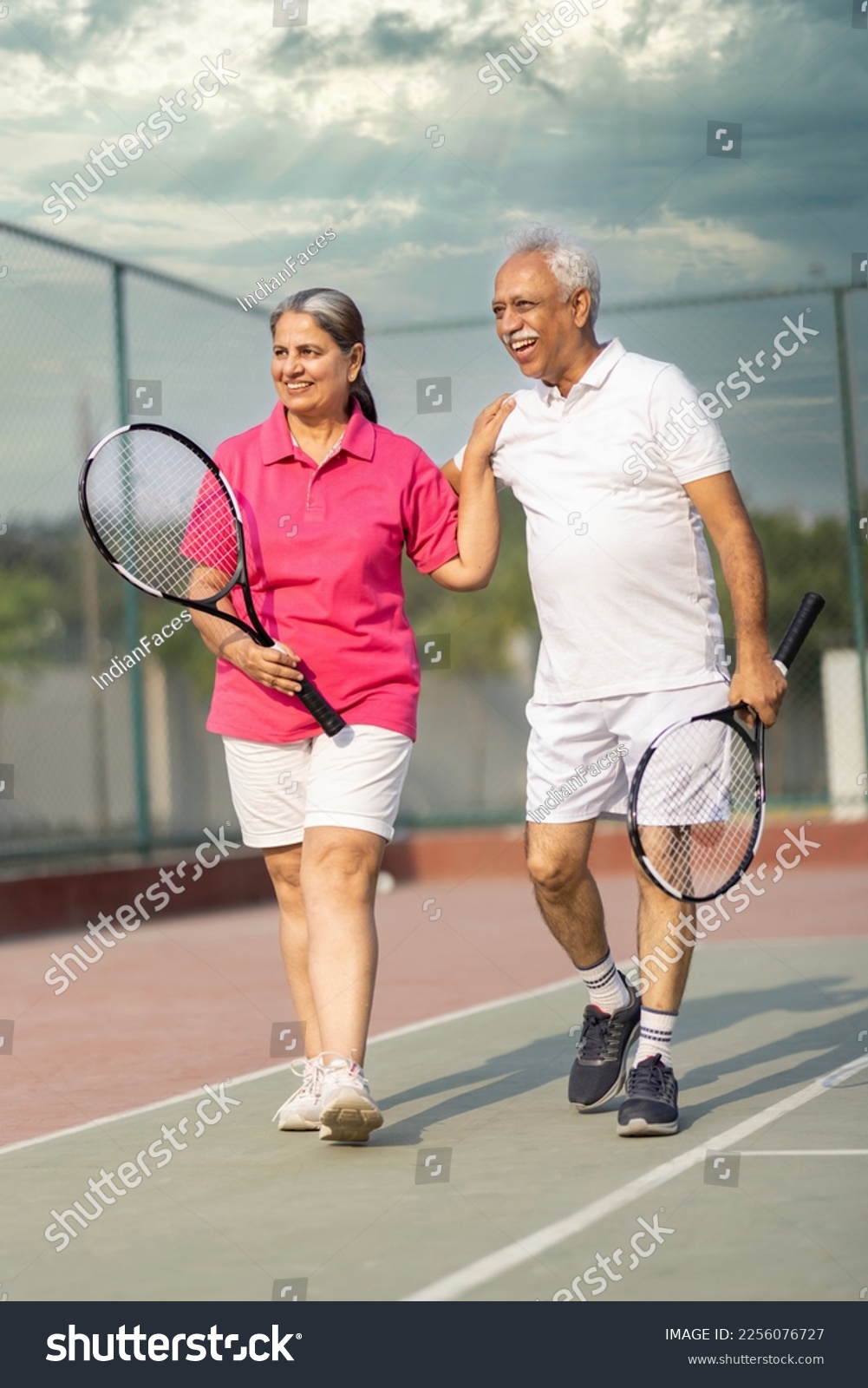 Senior man and woman hugging after playing a game of tennis at an outdoor court. #2256076727
