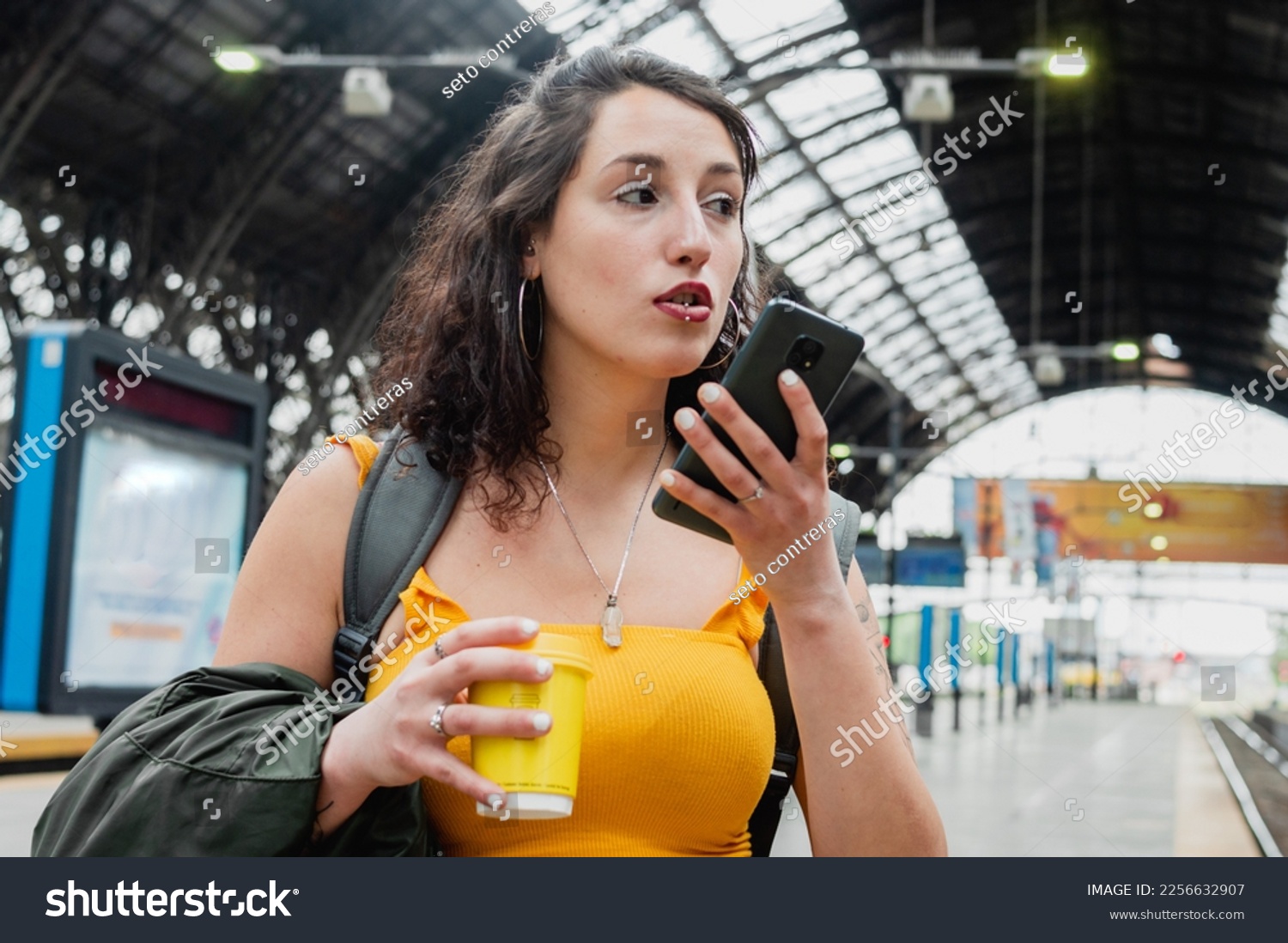 young latin woman of argentinian ethnicity, is worried at the train station stop sending a voice message on the phone, solving a problem with the trip. #2256632907