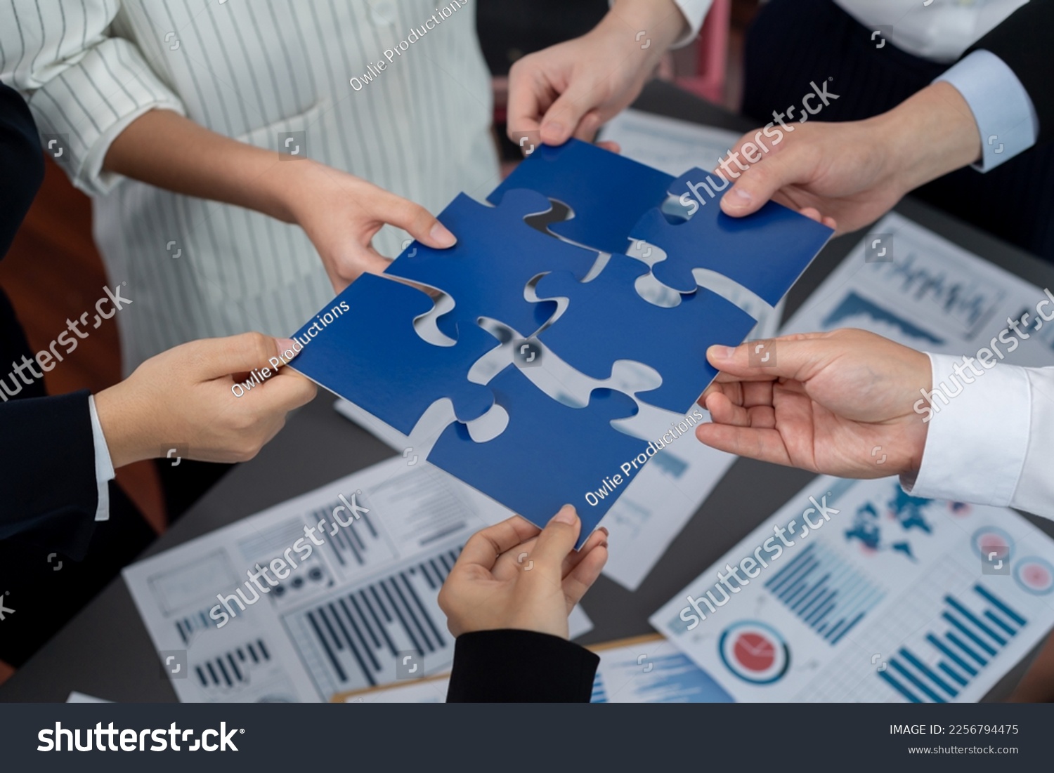 Closeup top view business team of office worker putting jigsaw puzzle together over table filled with financial report paper in workplace with manager to promote harmony concept in meeting room. #2256794475