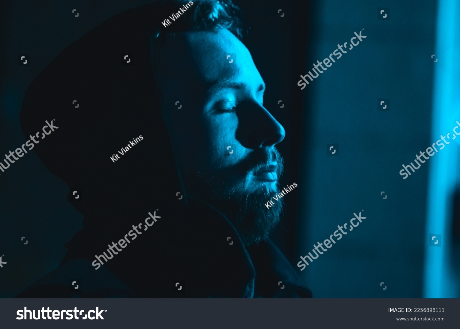 Portrait of smoking handsome man in a hood at the dark with cold blue light. Night life young man in a neon modern city. #2256898111