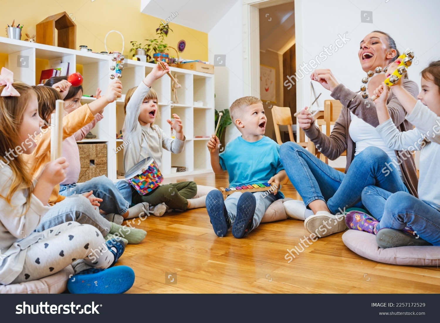Kindergarten teacher with children sitting on the floor having music class, using various instruments and percussion. Early music education #2257172529