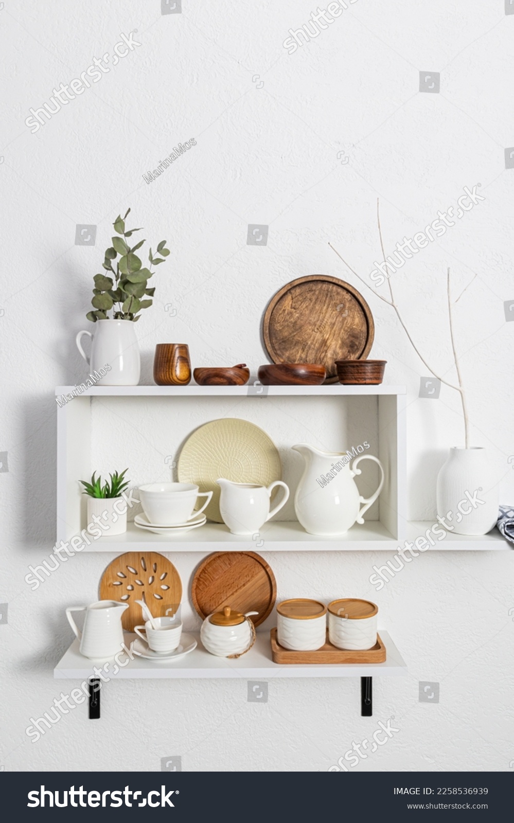 A set of white stylish open shelves with various ceramic white dishes, eco-friendly wooden dishes. white textured wall. kitchen without waste #2258536939