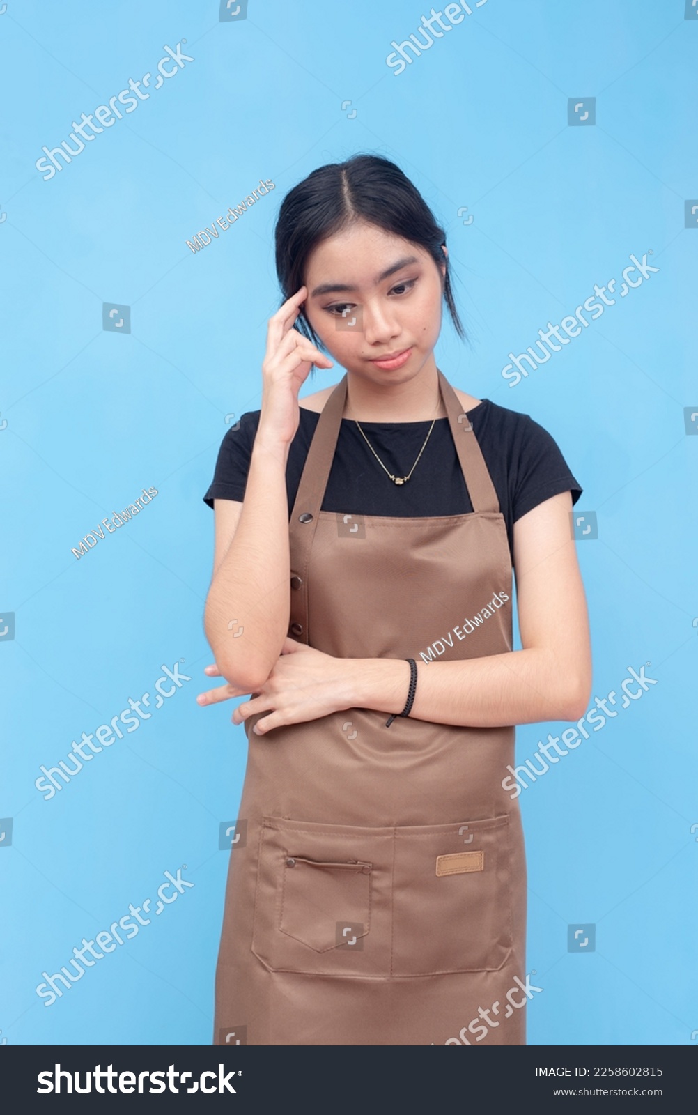 A cute and pretty asian barista or waitress in deep thought, worried about her job. Isolated on a light blue background. #2258602815