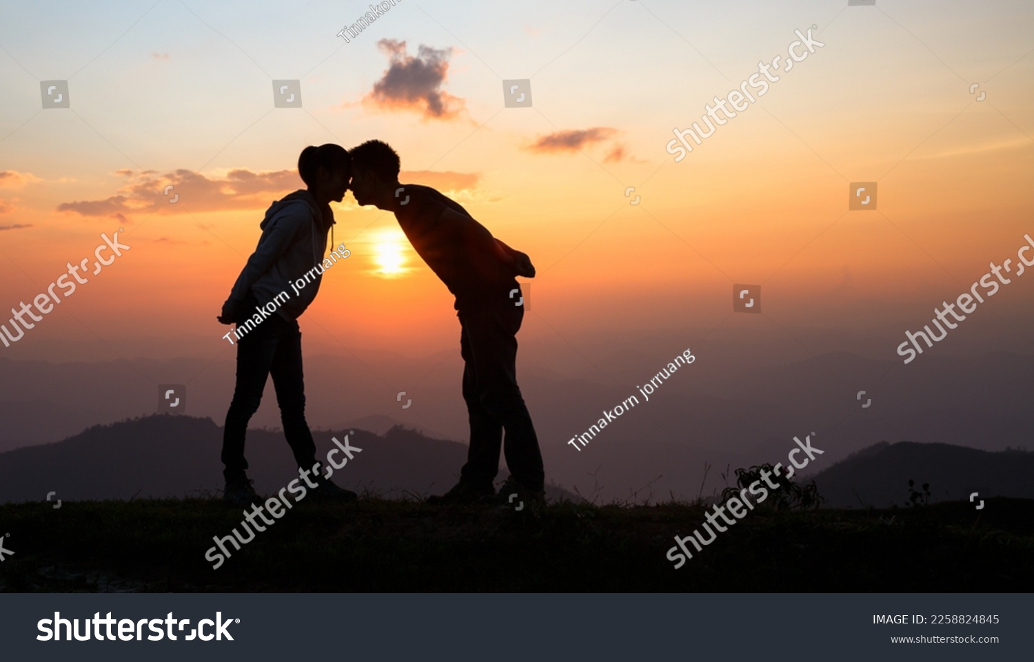 Silhouette of a couple on the mountain, A young romantic couple enjoy a beautiful view of the sun setting over the mountains, love, Valentine's Day. #2258824845