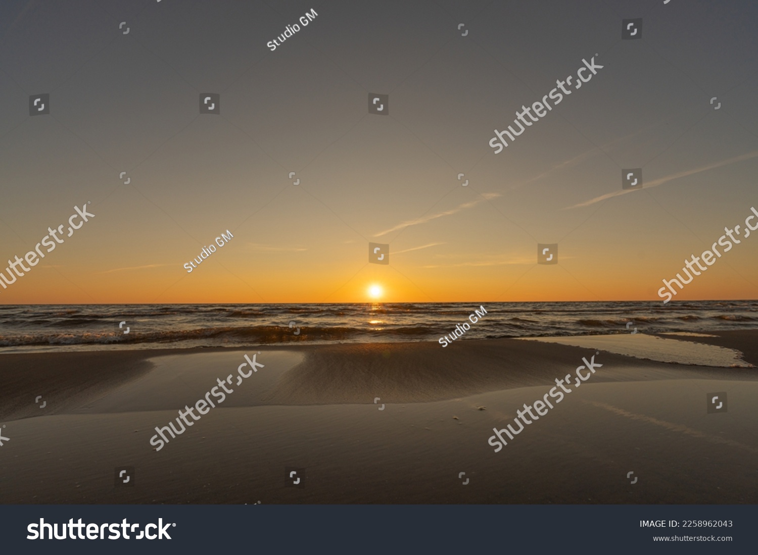 Sunset in a cloudless sky on the coast of the Gulf of Finland in Ust-Narva. The sky is clear, the waves gently roll on the sand. Estonia, Narva-Jyesuu. Natural background. Space for text. #2258962043