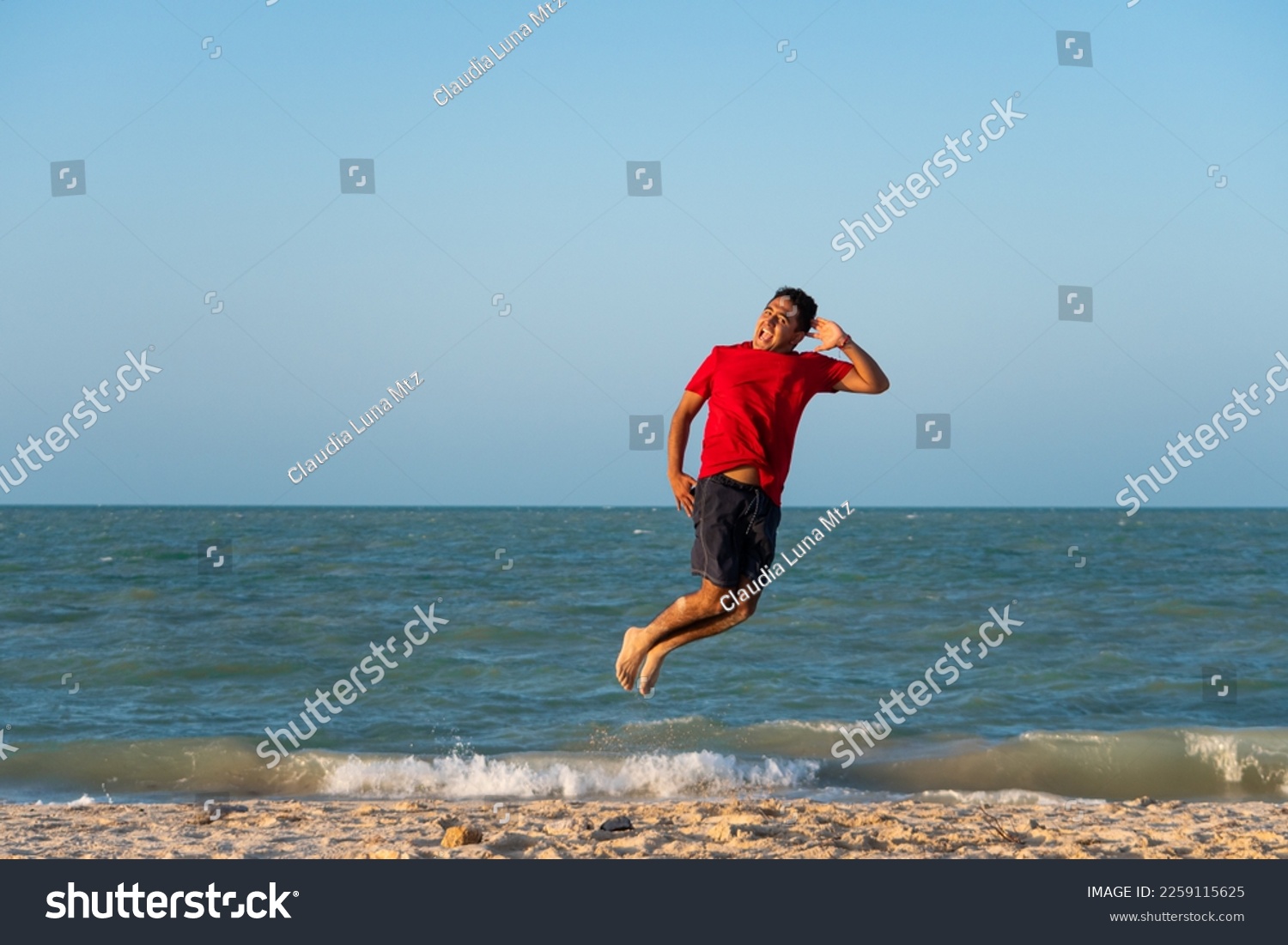young latin man jumping on the shore of the beach #2259115625