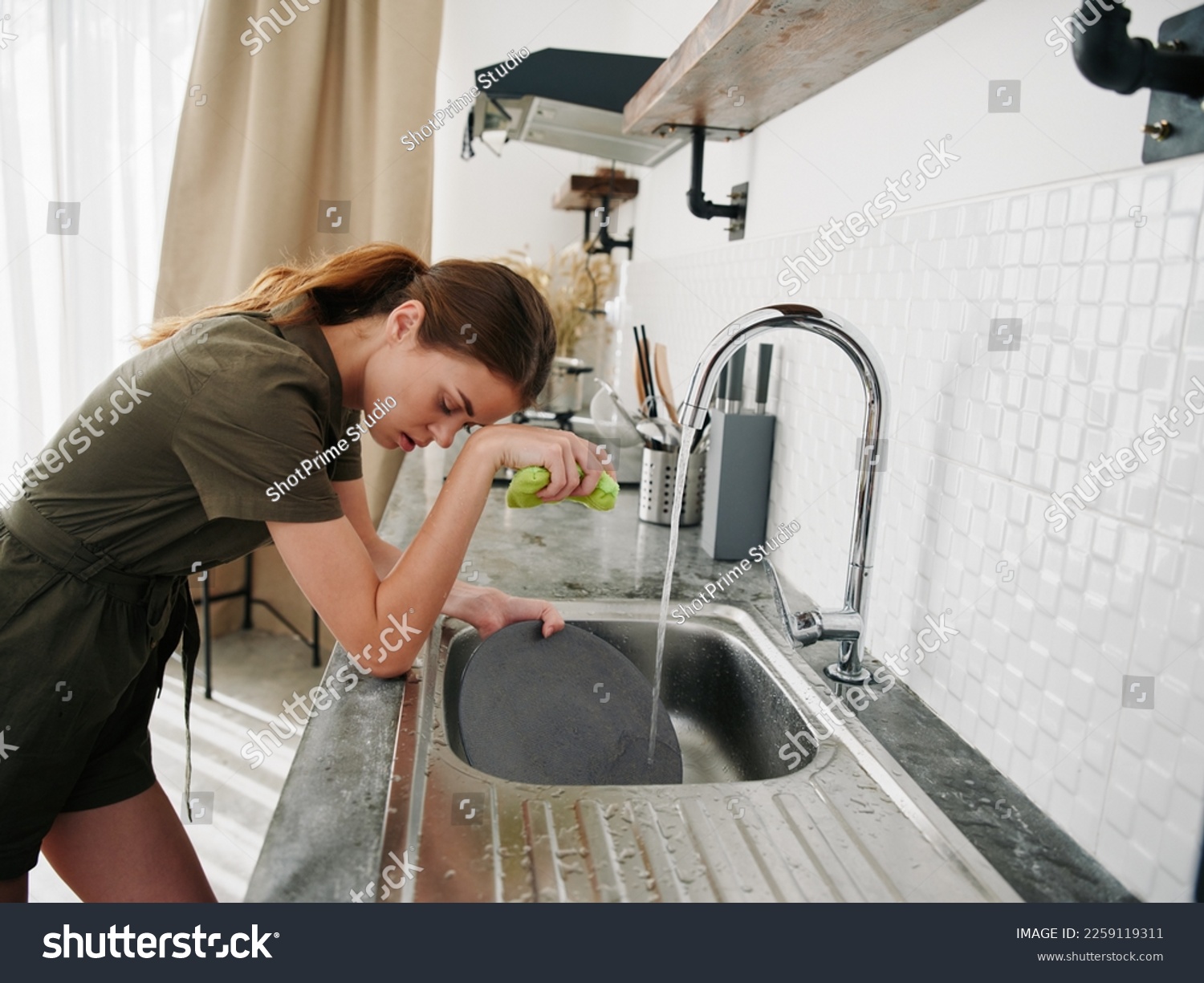 Woman tired and angry hands without gloves washes dishes with a dishwashing sponge, household chores, no dishwasher, high water consumption. Stylish kitchen design #2259119311