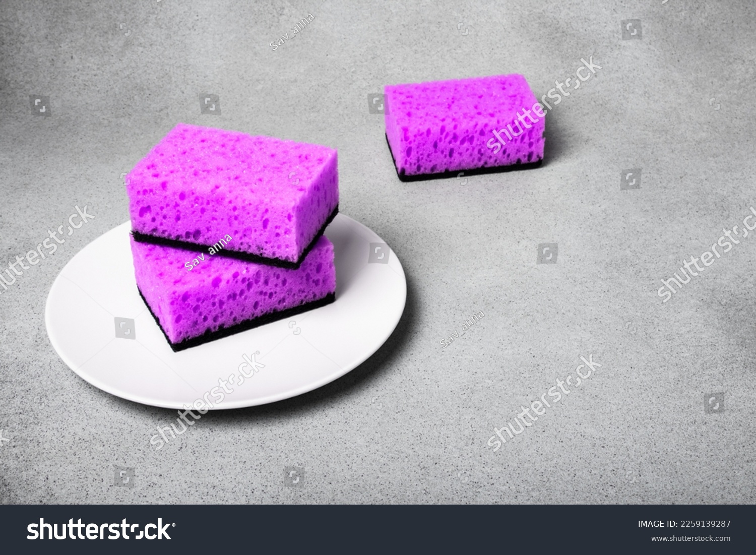Lilac sponges for dishwashing on a white plate on a neutral gray background. Gentle dishwashing. House cleaning #2259139287