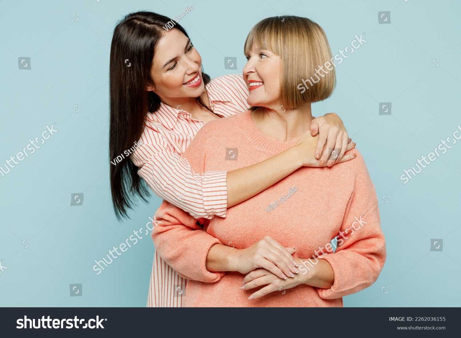 Cheerful fun satisfied elder parent mom with young adult daughter two women together wearing casual clothes hugging cuddle look to each other isolated on plain blue cyan background. Family day concept #2262036155